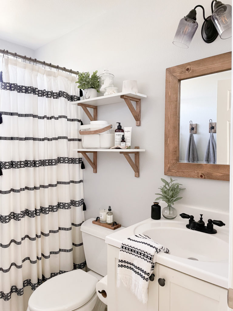 Bathroom makeover - Pulled back view of the updated bathroom Vanity, faucet, Mirror, shower curtain, and shelves. 