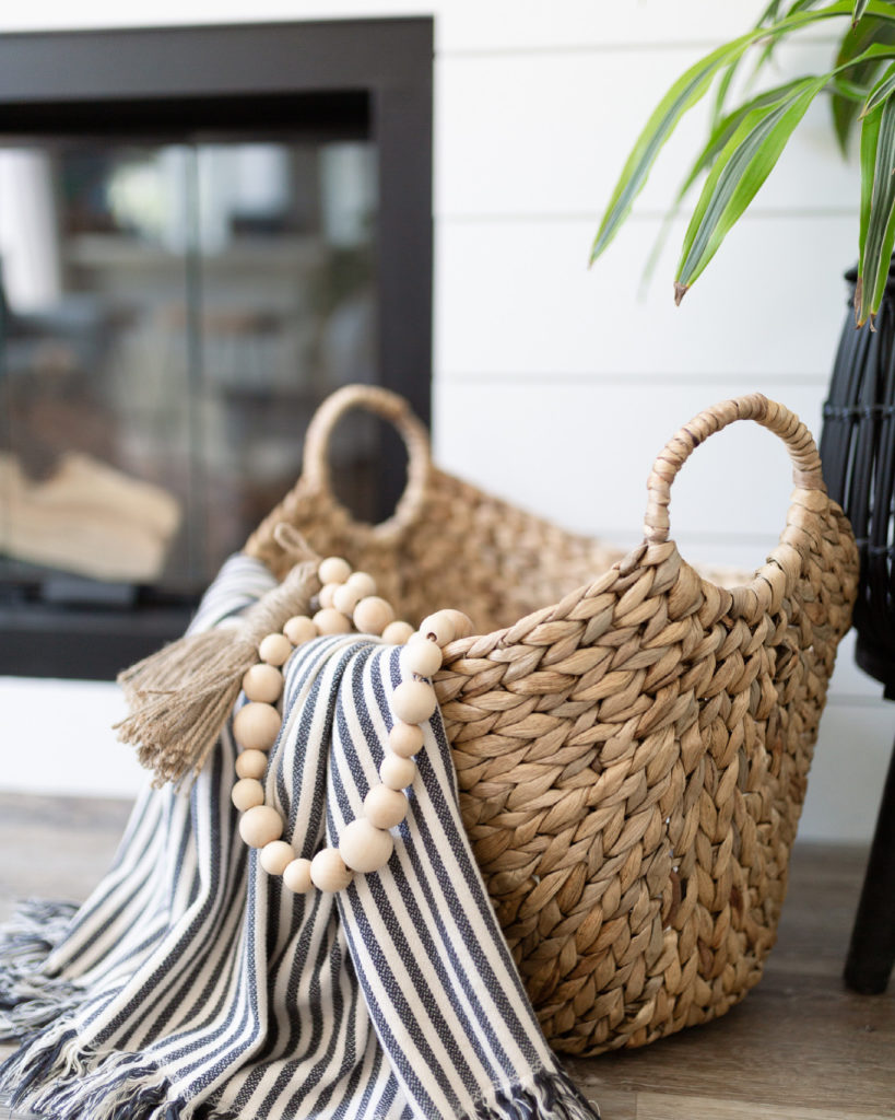 Closeup view of the decor in front of the fireplace. A boat basket (from Walmart) with striped throw (from Ikea) and wooden beads (from Hobby lobby) 